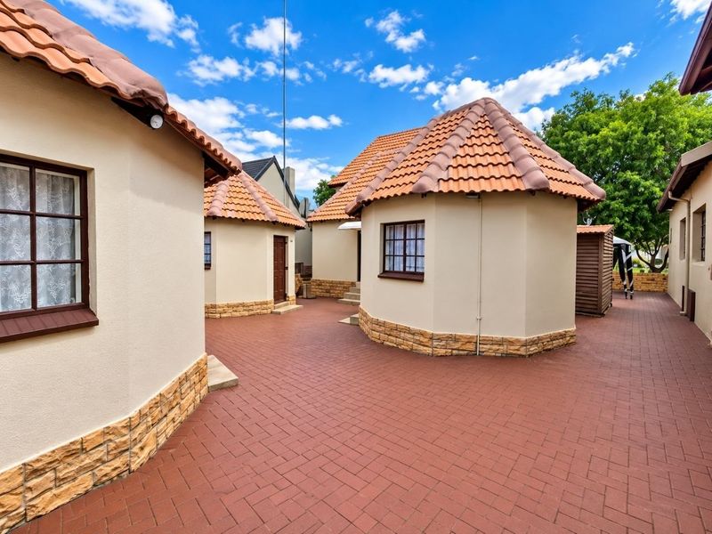 A well-maintained rear courtyard featuring multiple structures with terracotta tiled roofs, stone cladding accents, and paved flooring.