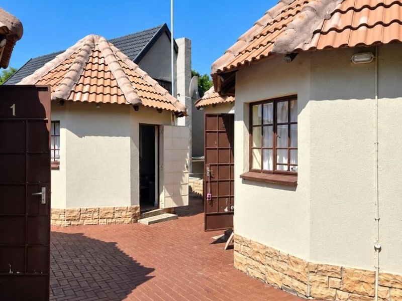 Exterior view of detached residential units featuring terracotta tiled roofs, stucco walls with stone cladding, and a paved courtyard area.