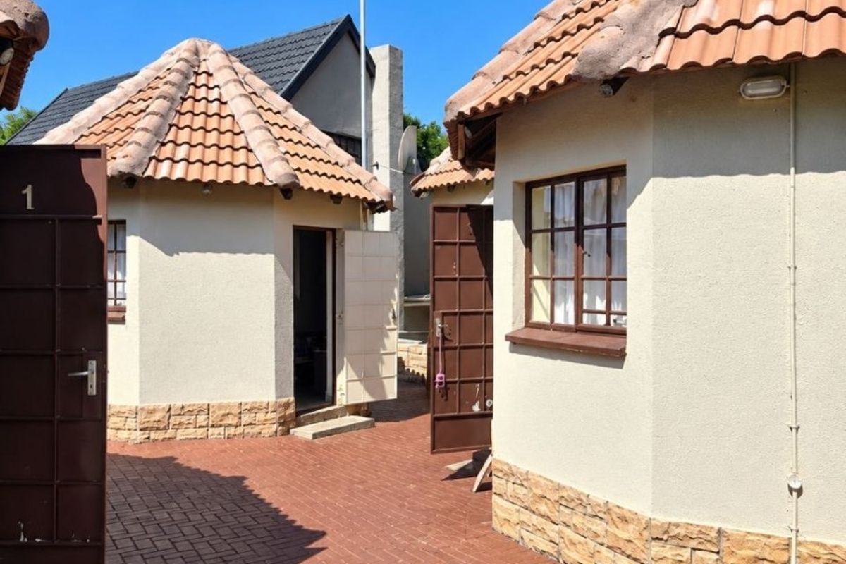 Exterior view of detached residential units featuring terracotta tiled roofs, stucco walls with stone cladding, and a paved courtyard area.