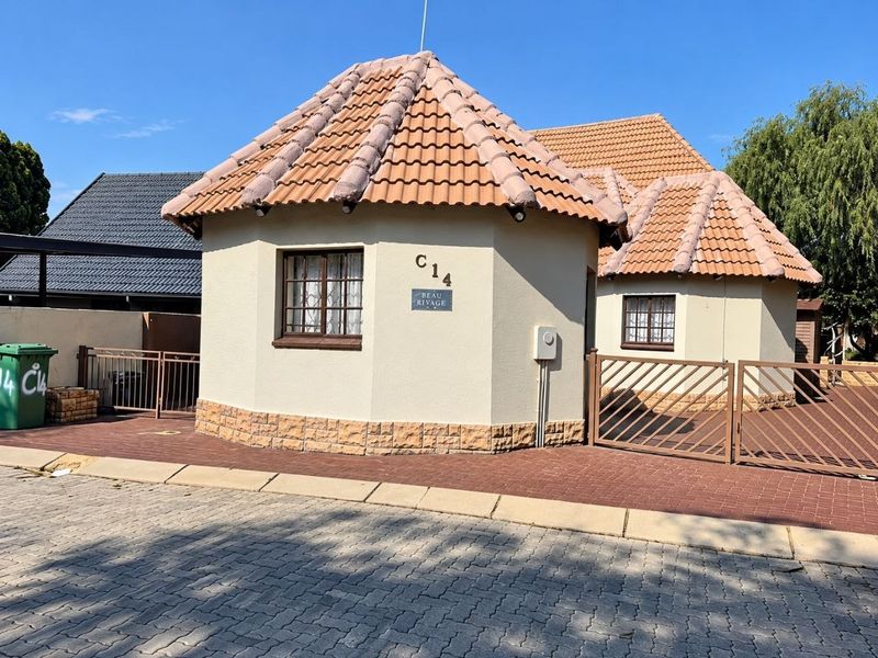 Front exterior view of a residential property featuring a unique tiled roof design, stone cladding accents, and a paved driveway with gated access.