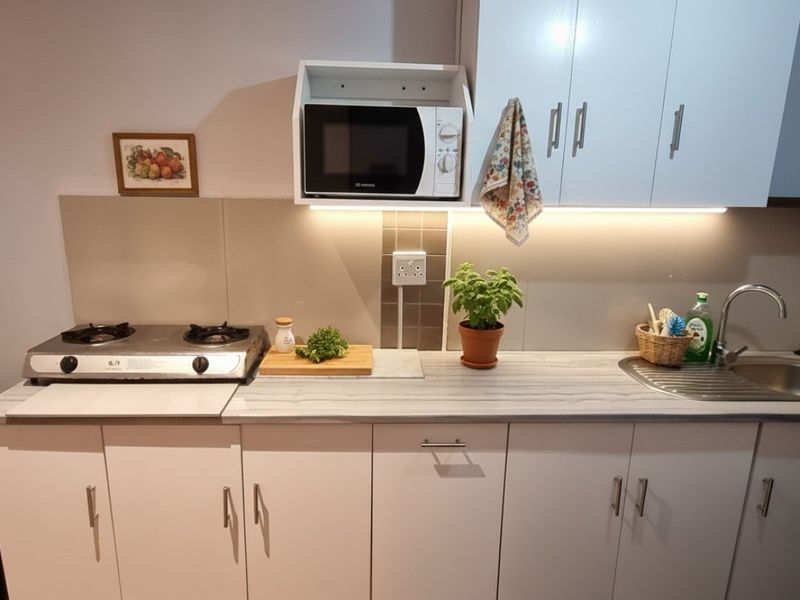 Compact kitchen featuring white cabinetry, laminate countertops, a stainless steel sink, gas hob, and integrated microwave with under-cabinet lighting.