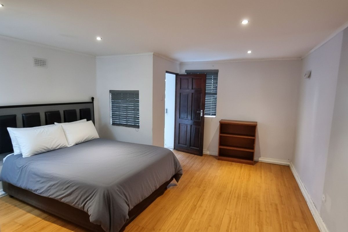 A spacious bedroom featuring laminate flooring, recessed downlighting, and venetian blinds, offering a clean and neutral living space.