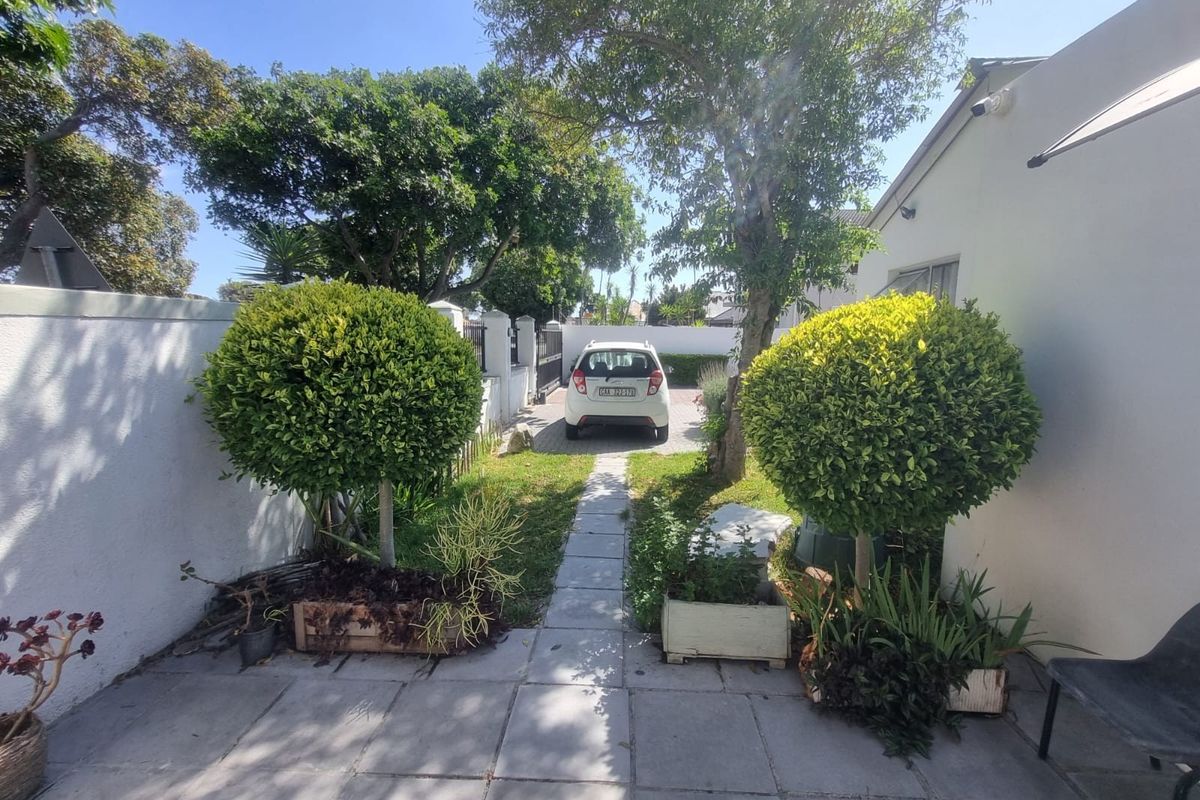 A rear exterior view of the cottage featuring a paved patio area, a central walkway, and established boundary walls.