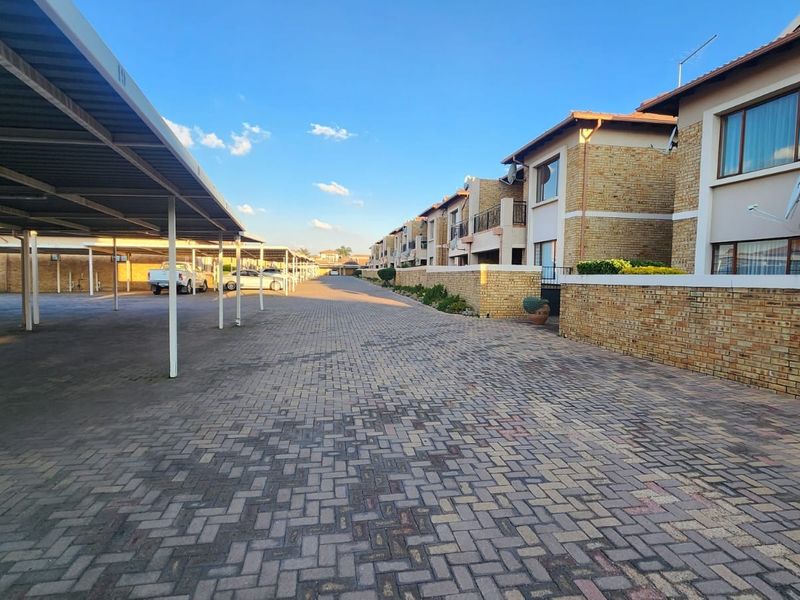 Exterior view of a townhouse complex featuring a paved driveway, covered parking bays, and facebrick building facades with balconies.