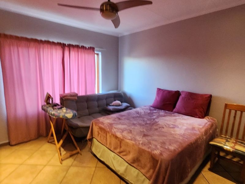 A bedroom featuring tiled flooring, a ceiling fan, and a built-in wardrobe, providing a functional space with neutral wall finishes.