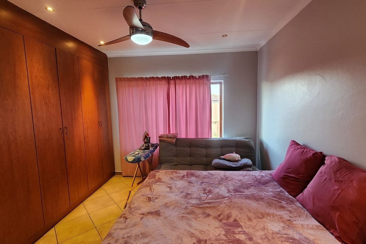 A bedroom featuring extensive built-in wooden cupboards, tiled flooring, and a ceiling fan, providing functional storage and climate control.