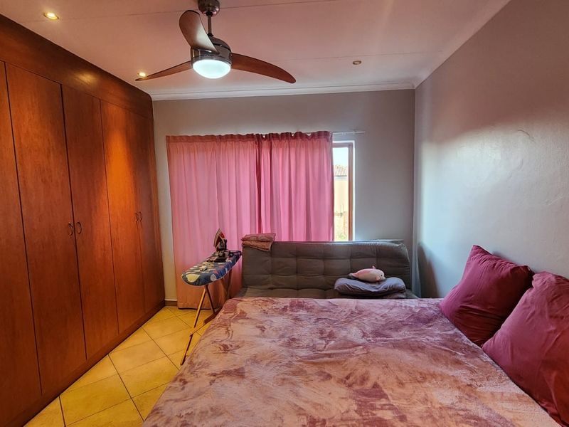 A bedroom featuring extensive built-in wooden cupboards, tiled flooring, and a ceiling fan, providing functional storage and climate control.