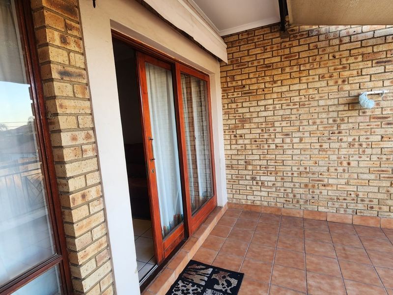 A covered patio area featuring exposed brick walls and tiled flooring, providing direct access to the interior through sliding wooden doors.