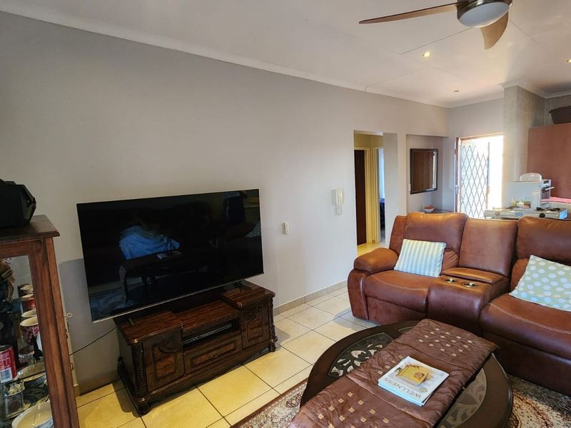A comfortable living room featuring tiled flooring, a ceiling fan, and recessed lighting, with an open-plan layout leading towards the kitchen area.