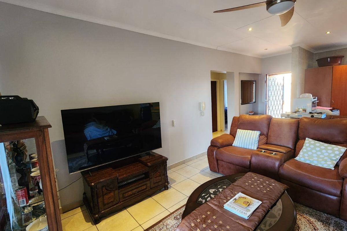 A comfortable living room featuring tiled flooring, a ceiling fan, and recessed lighting, with an open-plan layout leading towards the kitchen area.