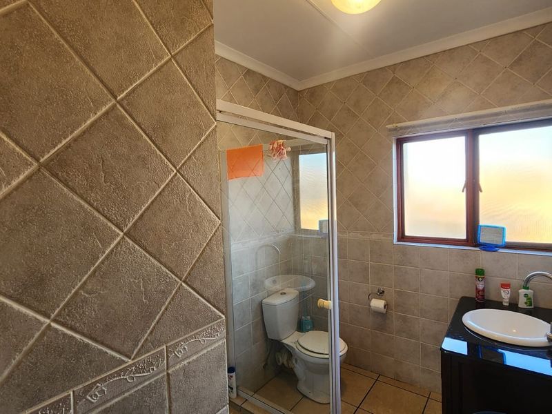 A functional bathroom featuring a shower enclosure, toilet, and a vanity basin with tiled walls and flooring throughout.