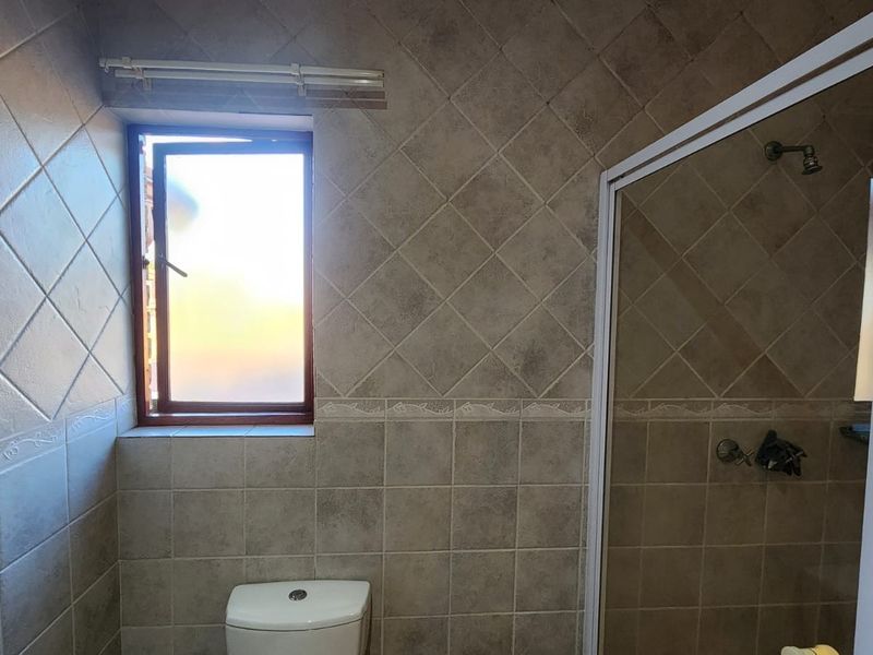 A functional bathroom featuring tiled walls, a shower enclosure, and a toilet, with a window providing natural light.