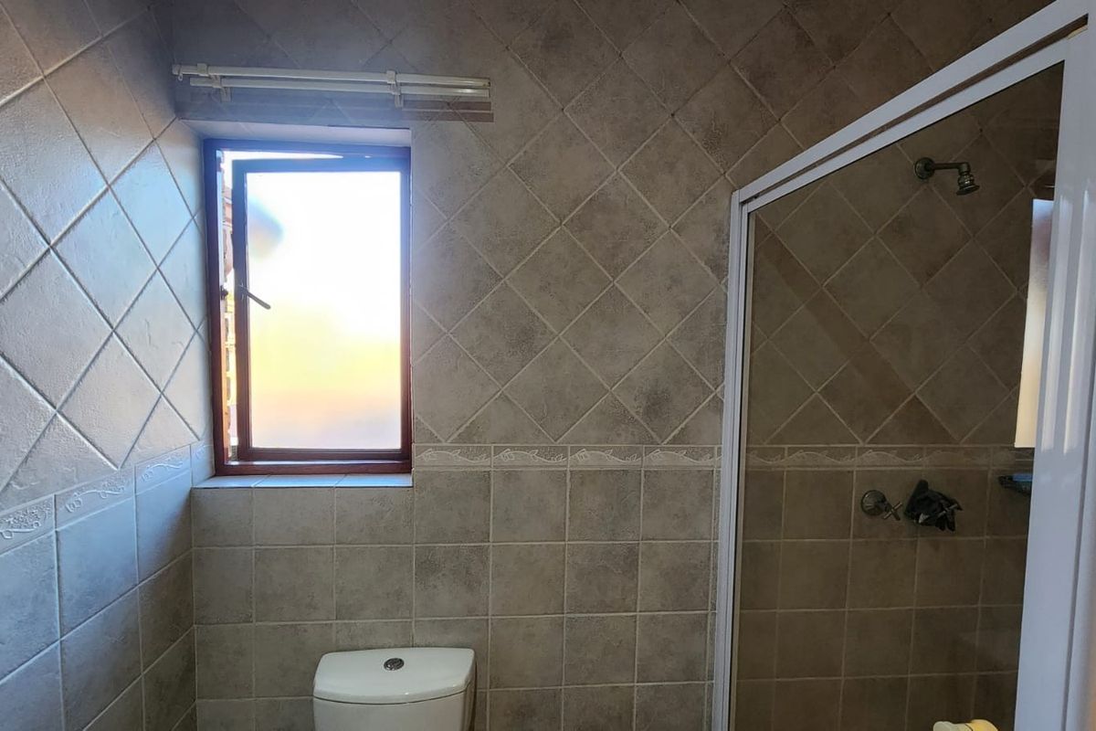 A functional bathroom featuring tiled walls, a shower enclosure, and a toilet, with a window providing natural light.