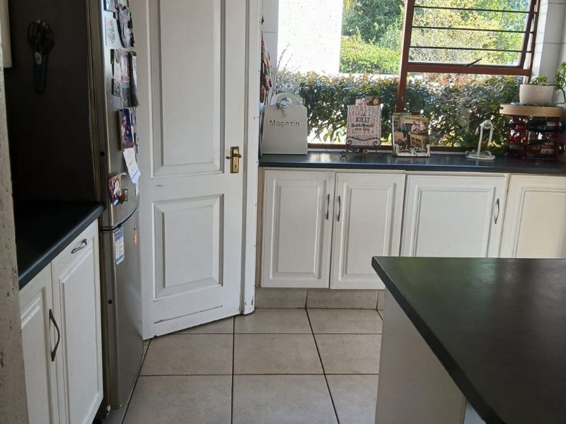 A functional kitchen featuring white cabinetry, dark countertops, tiled flooring, and a window with security bars overlooking the garden.