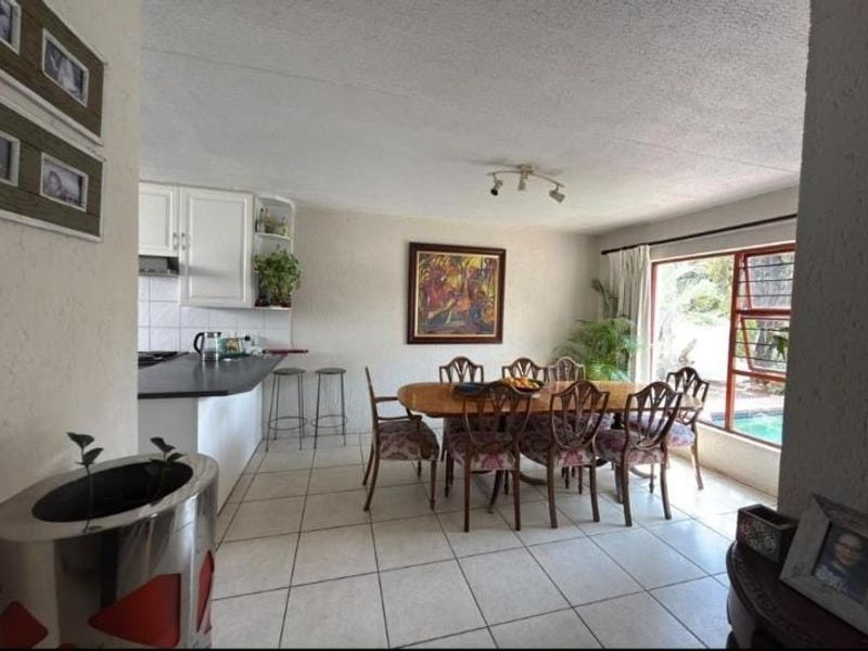 Open plan kitchen and dining area featuring tiled flooring, built-in cabinetry, and large windows providing natural light and views of the outdoor pool area.