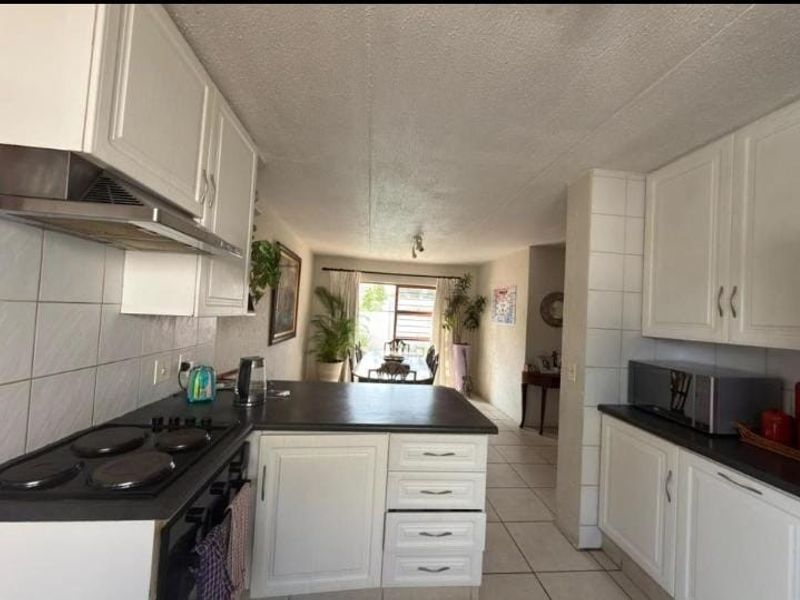 Open-plan kitchen and dining area featuring white cabinetry, dark countertops, electric hob, and tiled flooring, creating a functional and connected living space.