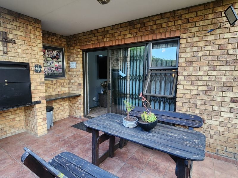 Covered patio area featuring a built-in braai, tiled flooring, and direct access to the interior through a sliding glass door with security gate.