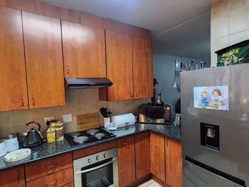 A functional kitchen featuring wood-finish cabinetry, granite countertops, a built-in oven, and an electric hob with an extractor fan.