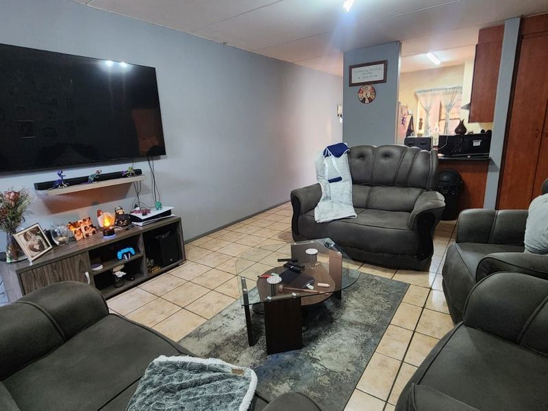 Open plan living area featuring tiled flooring and a view into the adjacent kitchen with built-in cabinetry.