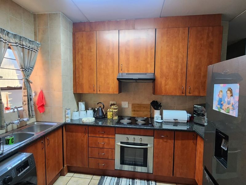 A functional kitchen featuring warm-toned wooden cabinetry, granite countertops, a built-in oven with hob, and a double basin sink with tiled backsplash.