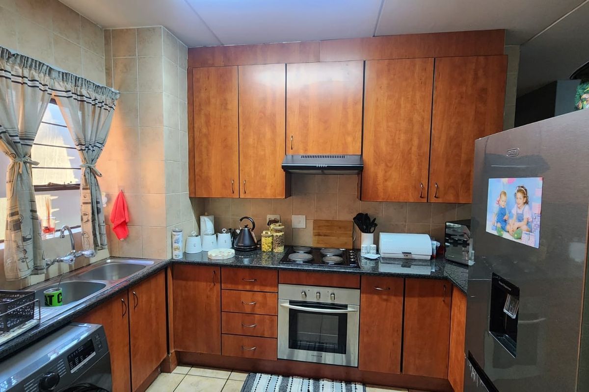 A functional kitchen featuring warm-toned wooden cabinetry, granite countertops, a built-in oven with hob, and a double basin sink with tiled backsplash.