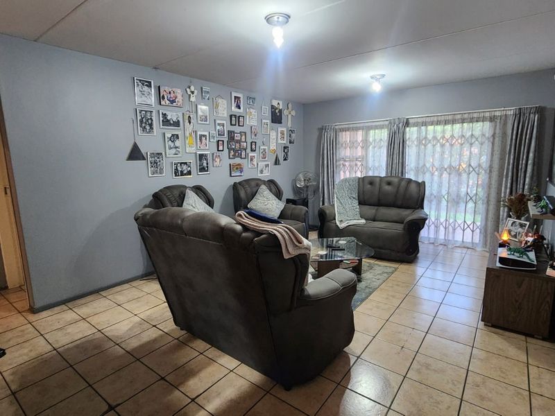 A spacious living room featuring tiled flooring and a sliding glass door with security gate, providing access to the exterior.