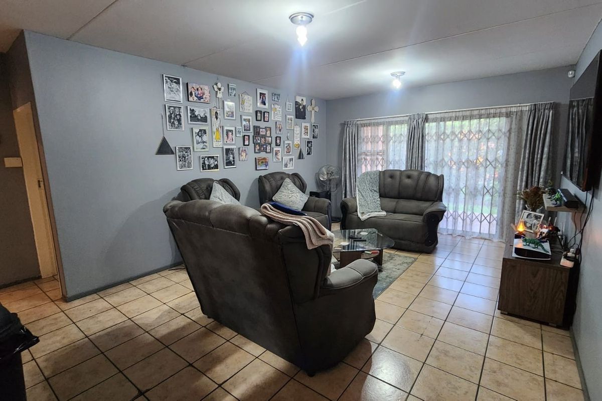 A spacious living room featuring tiled flooring and a sliding glass door with security gate, providing access to the exterior.