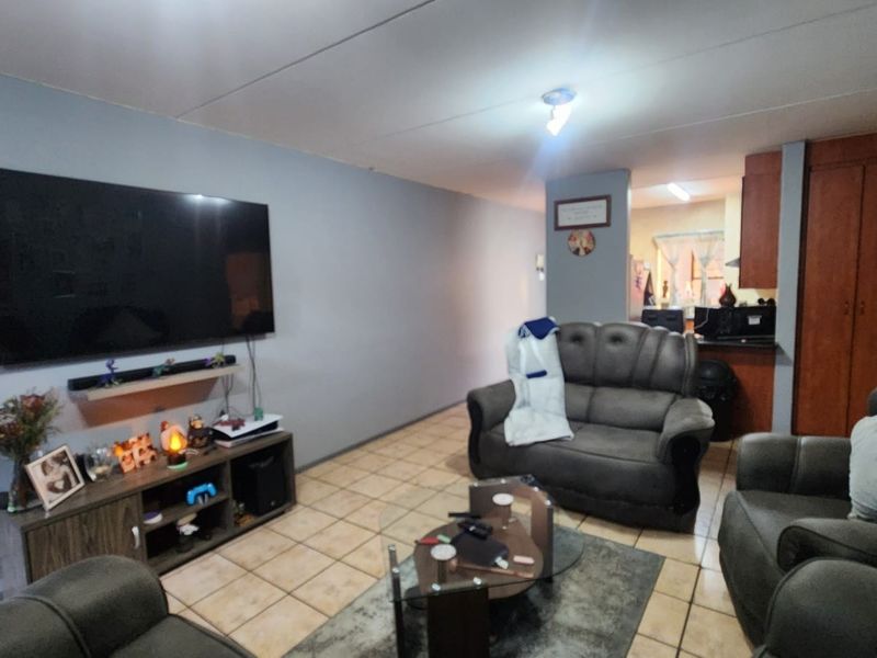 Open plan living area featuring tiled flooring and a view into the adjacent kitchen space with built-in cabinetry.