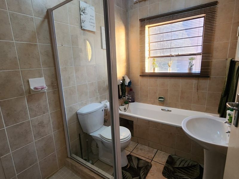 A functional bathroom featuring a shower enclosure, bathtub, pedestal basin, and tiled finishes throughout.