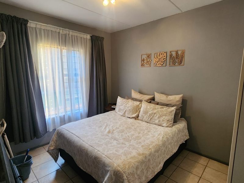 A functional bedroom featuring tiled flooring, a built-in wardrobe, and a window fitted with security bars.