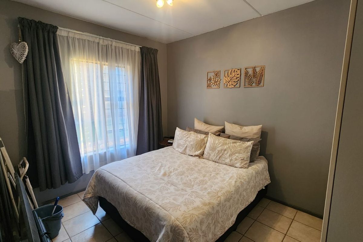 A functional bedroom featuring tiled flooring, a built-in wardrobe, and a window fitted with security bars.