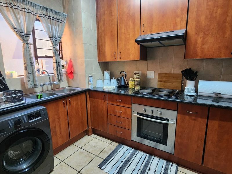 A functional kitchen featuring warm-toned wooden cabinetry, granite countertops, a built-in oven with hob, and integrated laundry plumbing.