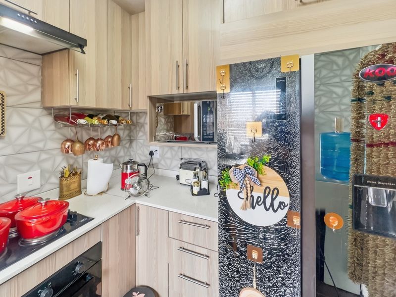 Compact modern kitchen featuring light wood-grain cabinetry, stone countertops, a tiled backsplash, and integrated cooking appliances.