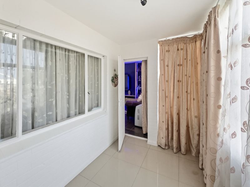 A bright, enclosed patio or sunroom featuring tiled flooring, painted brick walls, and large windows, providing a versatile transition space to the interior living area.