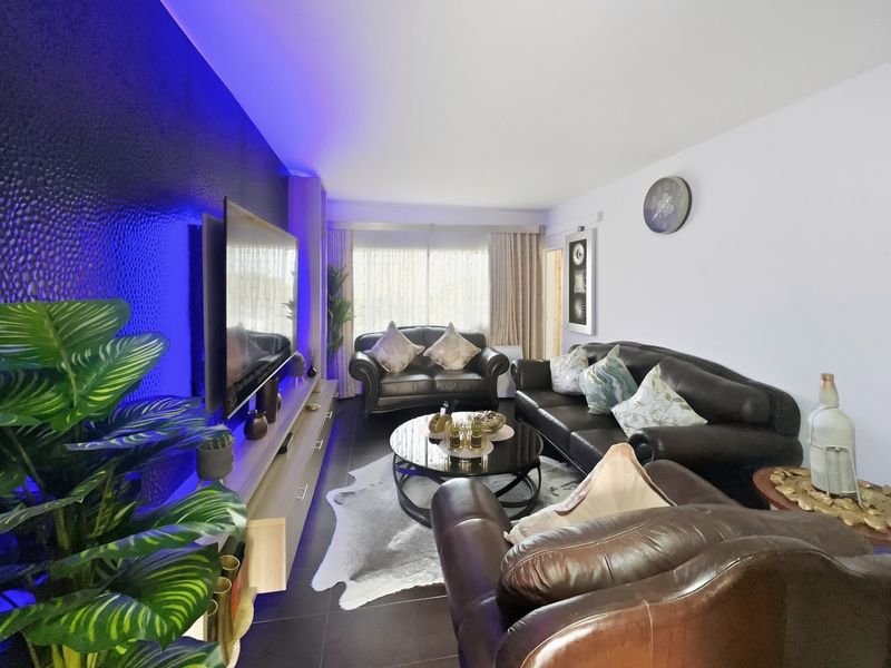 A modern living room featuring a textured accent wall with integrated blue LED lighting and dark tiled flooring.