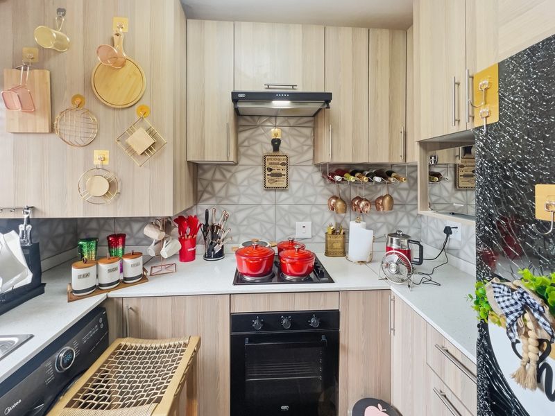 A compact, modern kitchen featuring light wood-grain cabinetry, stone countertops, a geometric tiled backsplash, and integrated appliances including an oven and hob.