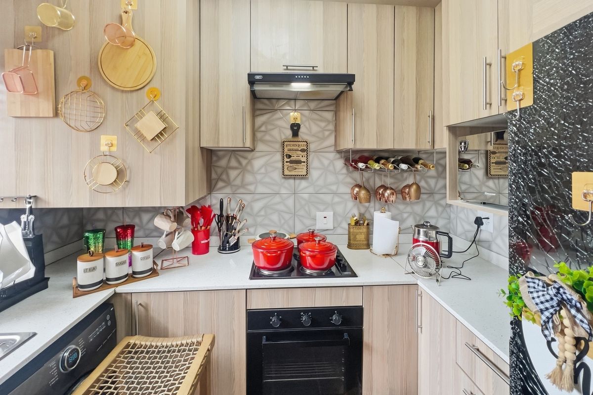 A compact, modern kitchen featuring light wood-grain cabinetry, stone countertops, a geometric tiled backsplash, and integrated appliances including an oven and hob.