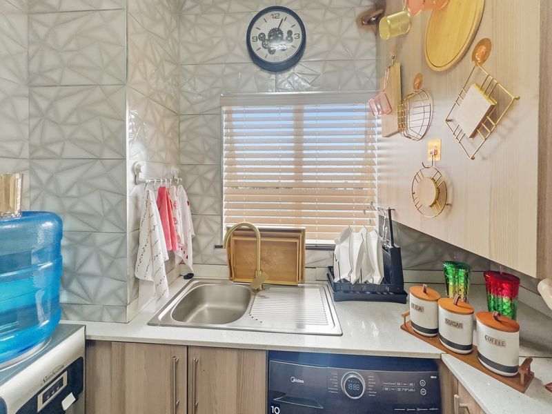 A compact, modern kitchen area featuring textured wall tiles, a stainless steel sink with a gold faucet, and integrated cabinetry with a built-in washing machine.