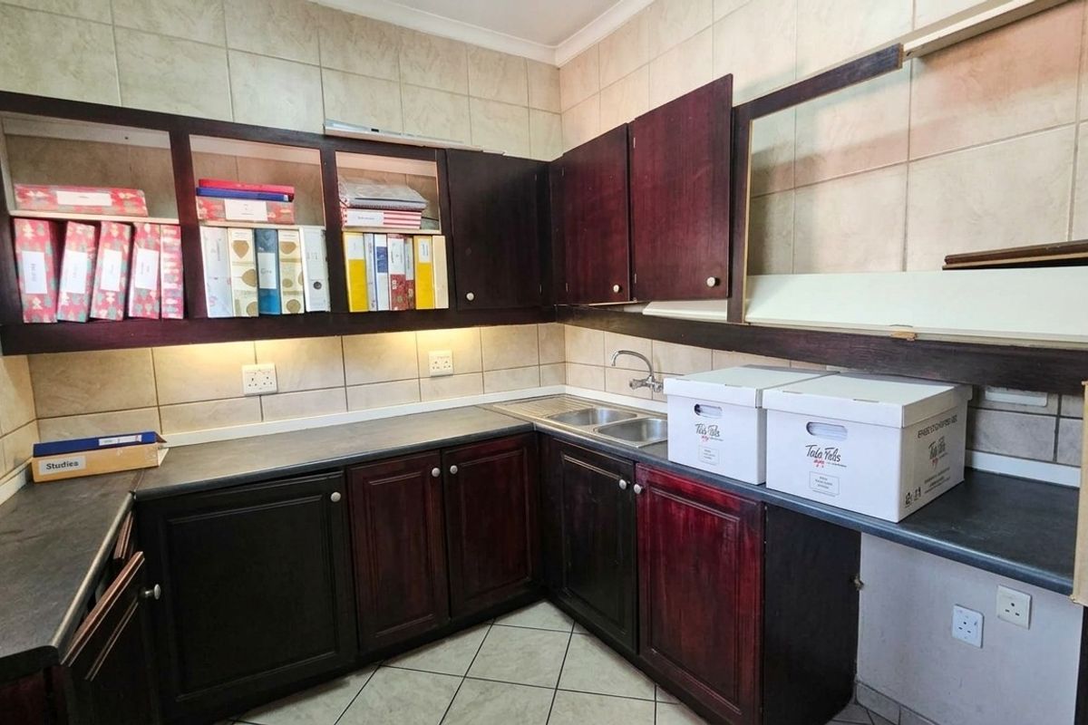 A functional kitchenette featuring dark wood cabinetry, laminate countertops, a stainless steel double sink, and tiled backsplash with under-cabinet lighting.