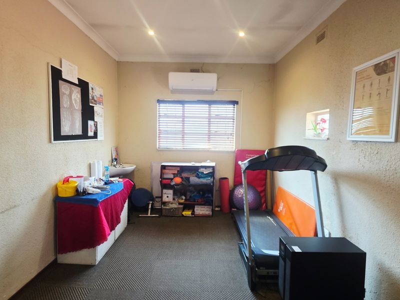 A functional office or consultation room featuring a built-in basin, wall-mounted air conditioning, and carpeted flooring, suitable for professional or clinical use.