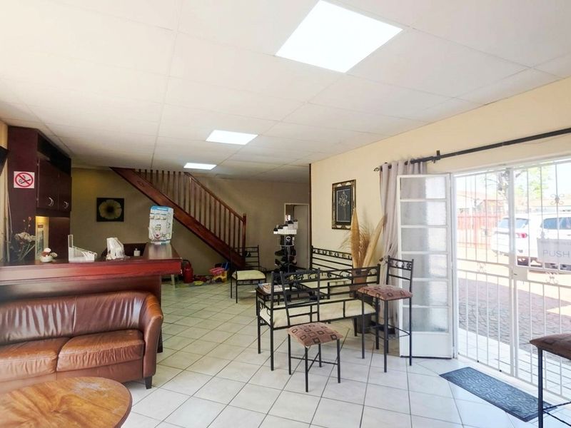 Open-plan office space featuring a reception counter, tiled flooring, recessed lighting, and a staircase leading to the upper level.