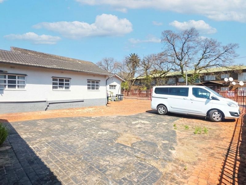 Rear exterior view of the office property featuring a paved driveway, perimeter fencing, and a tiled roof structure.