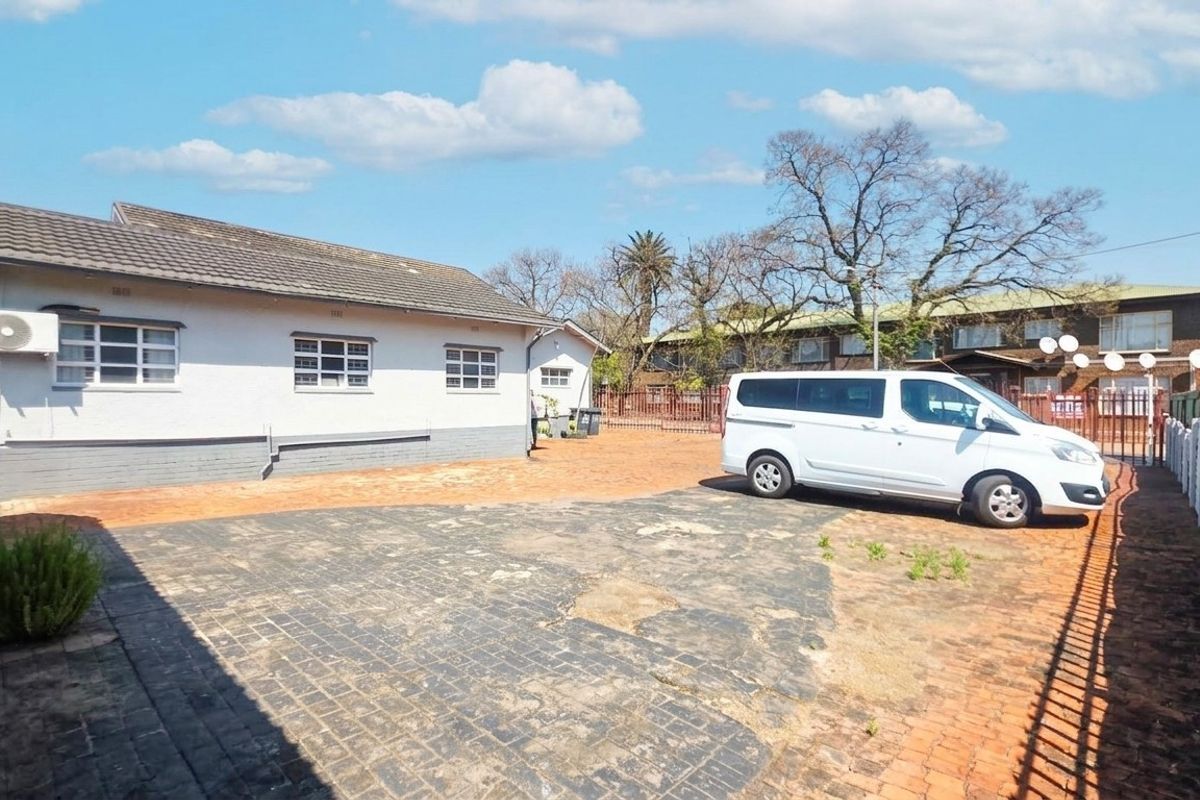Rear exterior view of the office property featuring a paved driveway, perimeter fencing, and a tiled roof structure.