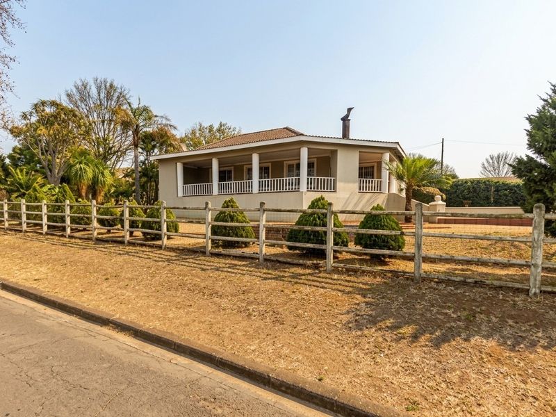 A front view of a single-story house featuring a covered veranda, tiled roof, and timber post-and-rail fencing along the street boundary.
