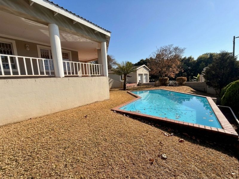 Outdoor pool area featuring a swimming pool with brick coping, adjacent to a covered patio and a detached garage structure.
