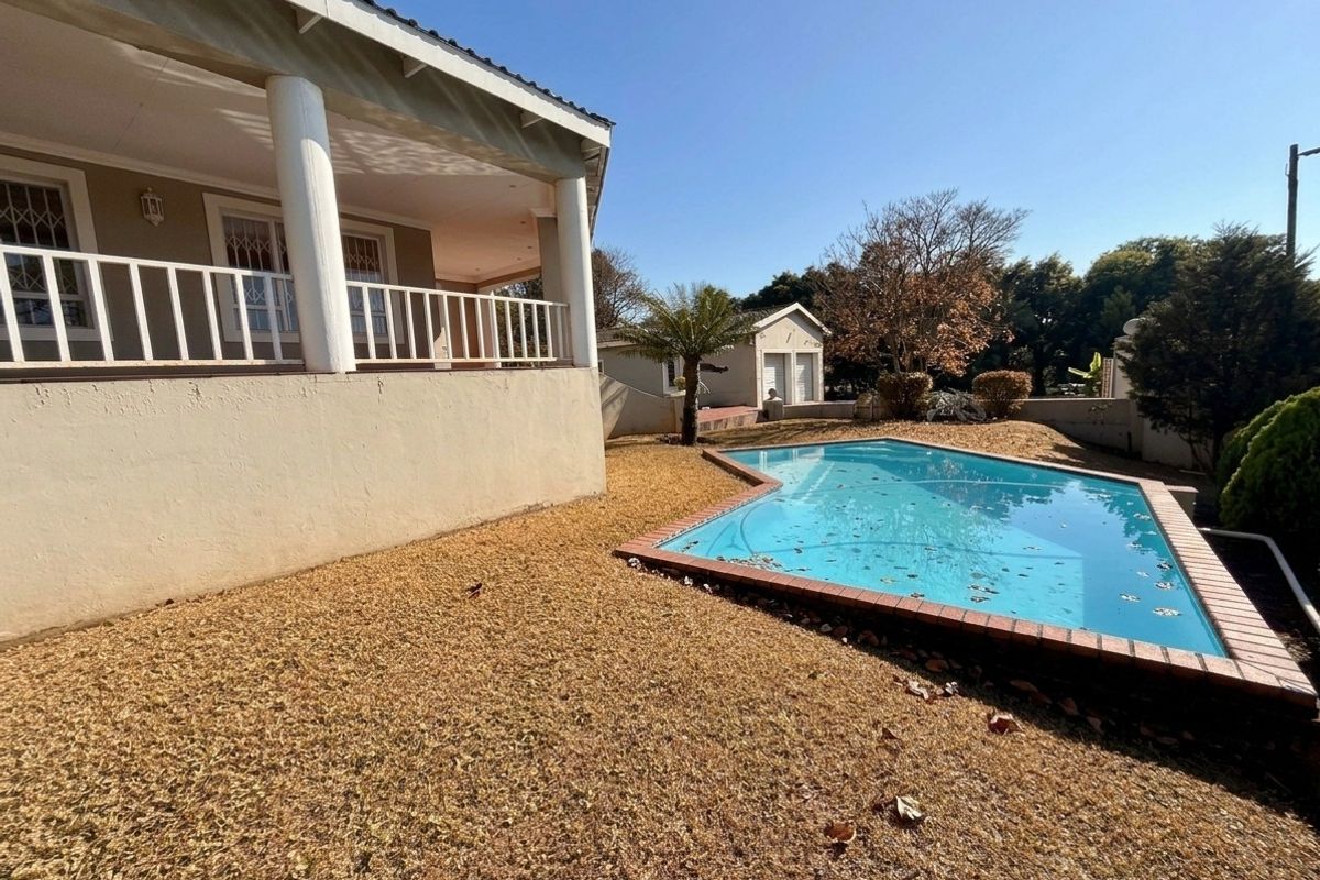 Outdoor pool area featuring a swimming pool with brick coping, adjacent to a covered patio and a detached garage structure.