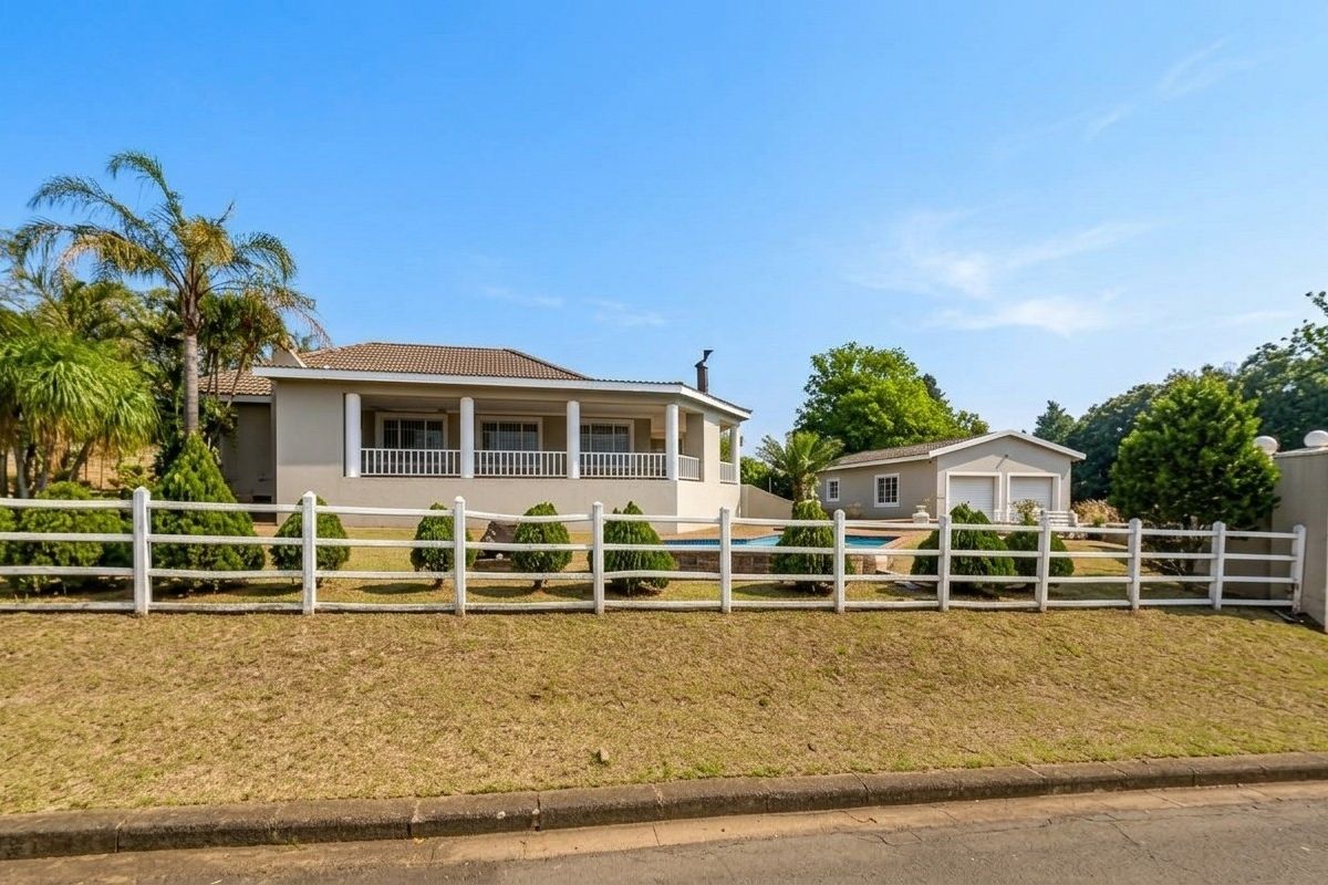 Rear view of the property featuring a covered patio, swimming pool, and a detached double garage set within a landscaped garden.