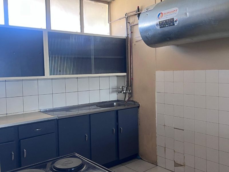 A functional kitchen featuring dark cabinetry, tiled splashbacks, a stainless steel sink, and an electric stove, with an exposed wall-mounted geyser.