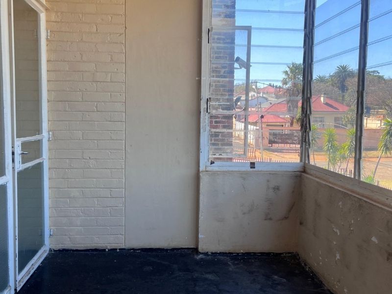 An enclosed balcony featuring louvre windows, painted brickwork, and a dark floor finish, offering a clear view of the surrounding neighborhood.