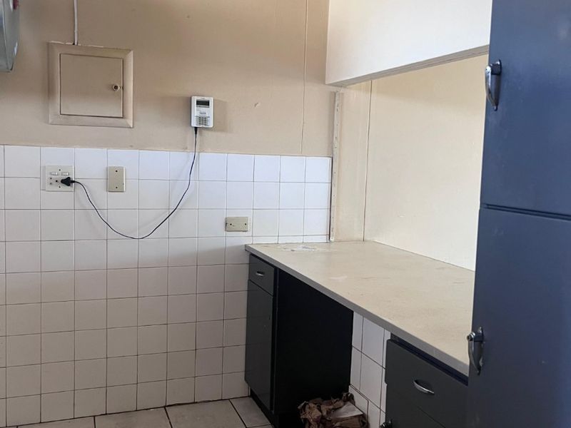 A functional scullery or utility area featuring tiled splashbacks, built-in cabinetry, and a laminate countertop, offering practical storage and workspace.